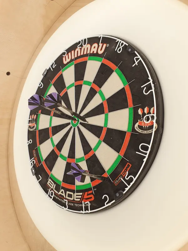 Professional dartboard with purple darts mounted on white surround in restaurant game area