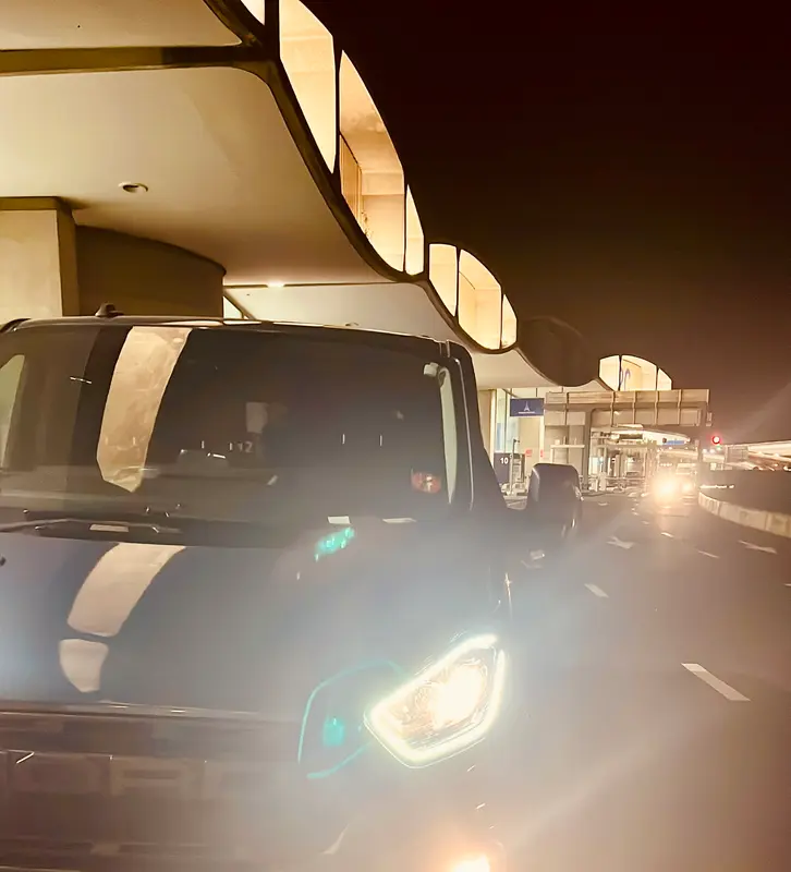 Nighttime airport terminal drop-off zone with vehicles lined up under illuminated curved architecture
