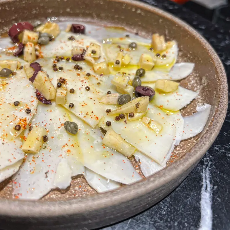 Celeriac carpaccio with capers, olives, mustard seeds, olive oil, and paprika in a rustic ceramic bowl