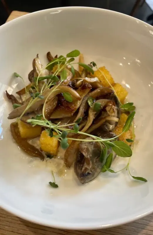 Sautéed wild mushrooms over crispy polenta cubes, garnished with fresh microgreens in a white bowl.