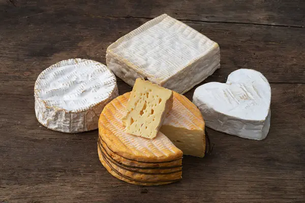 Assorted French cheeses including Camembert, Brie, heart-shaped, and washed-rind varieties on rustic wood board