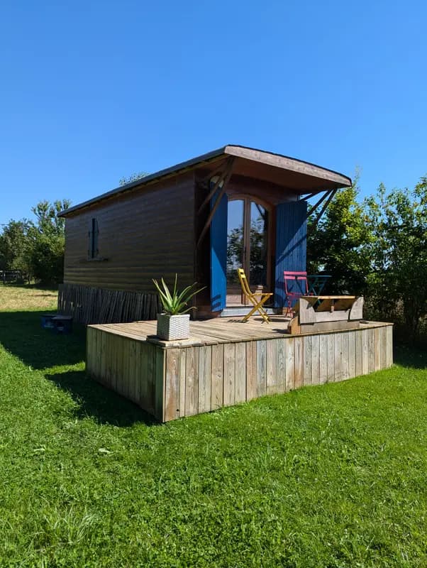 Rustic wooden cabin with blue shutters, colorful chairs on sunny deck surrounded by green countryside