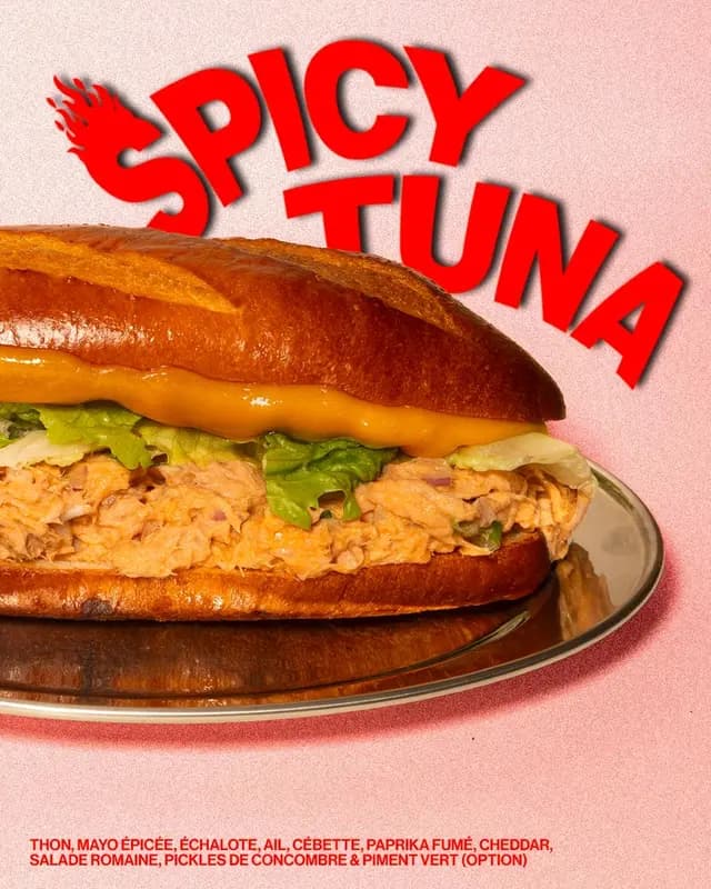 Spicy tuna sandwich on brioche bun with cheddar, romaine lettuce, spicy mayo, shallots, and smoked paprika on a silver plate.