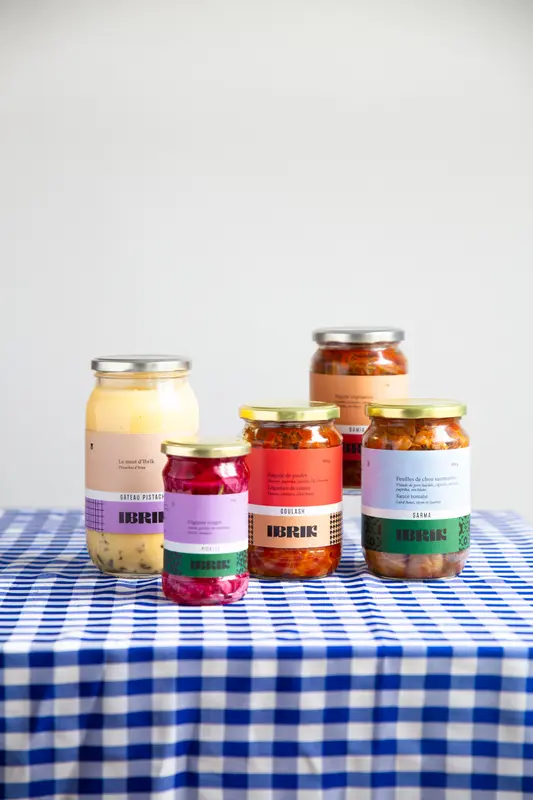Ibrik brand jarred foods including goulash, sarma, pickled onions, and pistachio cake on a blue gingham tablecloth