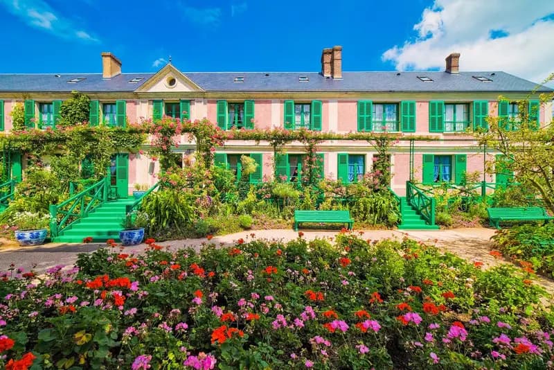 Charming pink French country restaurant with green shutters, lush flower gardens, and elegant outdoor seating in Giverny, France